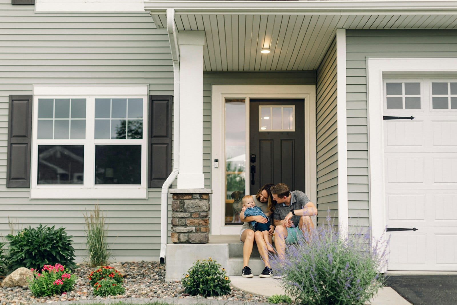 Young family sitting on the front steps of their new home, the kind of first home a guarantor home loan can help buy