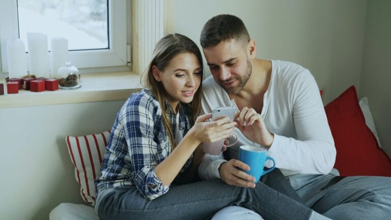 Couple on the couch reading news on a phone about the Suncorp Bank move to ANZ and what it means for their home loan