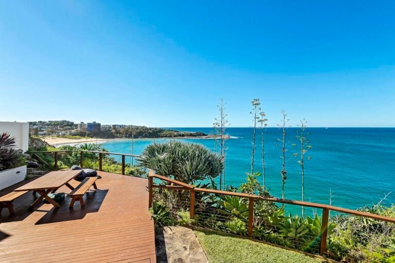 Sunny timber deck overlooking a beach, the kind of premium home upgraders can now reach in a two-tier property market